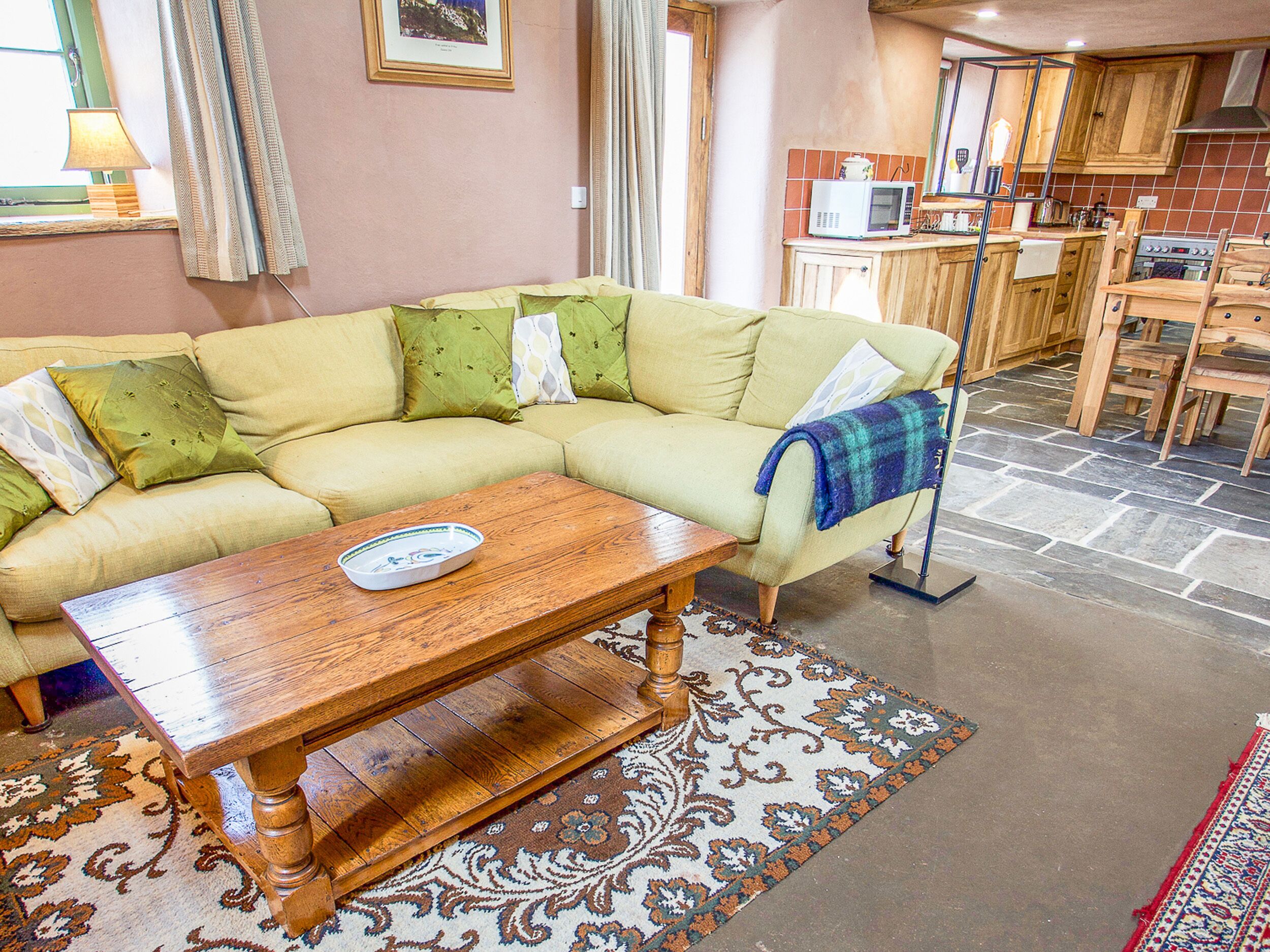 A living room with a sofa, a wooden coffee table, and a kitchen area with wooden cabinets and a microwave.