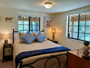A bedroom with a bed, two nightstands, a lamp, and a window with a view of trees.