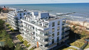 A modern multi-story building with balconies, located near a beach with a pier. - Apartamenty Sun & Snow Jantaris (Mielno)