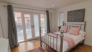 A bedroom with a bed, a metal headboard, a pink rug, and a view of the outside through a sliding door. - Wyvill House (Scarborough)