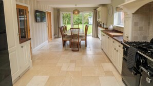A kitchen with a dining area, a TV mounted on the wall, and a view of the garden through the door. - Wyvill House (Scarborough)