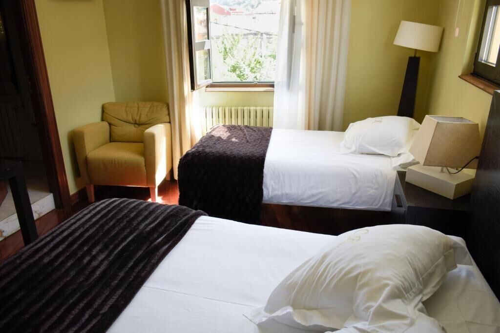Habitació d'hotel amb dos llits, una cadira, una làmpada i una finestra amb cortines.