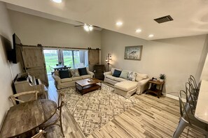 A spacious living room with a large wooden coffee table, two sofas, a dining table with chairs, and a ceiling fan.