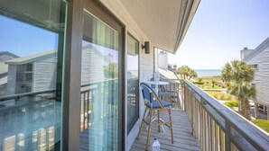 A balcony with a view of the ocean, a wooden deck, and two wicker chairs. - 300 Ocean Mile: 150 Steps to Beach! Kid Friendly, 2 Pools, Bikes! (Saint George Island)