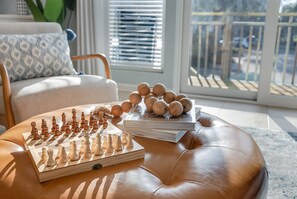 Relax in a comfortable chair with a patterned cushion, surrounded by a leather ottoman, a wooden chessboard, and a stack of books.
