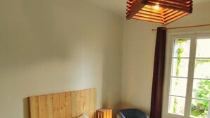 Een slaapkamer met een houten hoofdbord, een bed met witte lakens, een stoel en een raam met gordijnen.