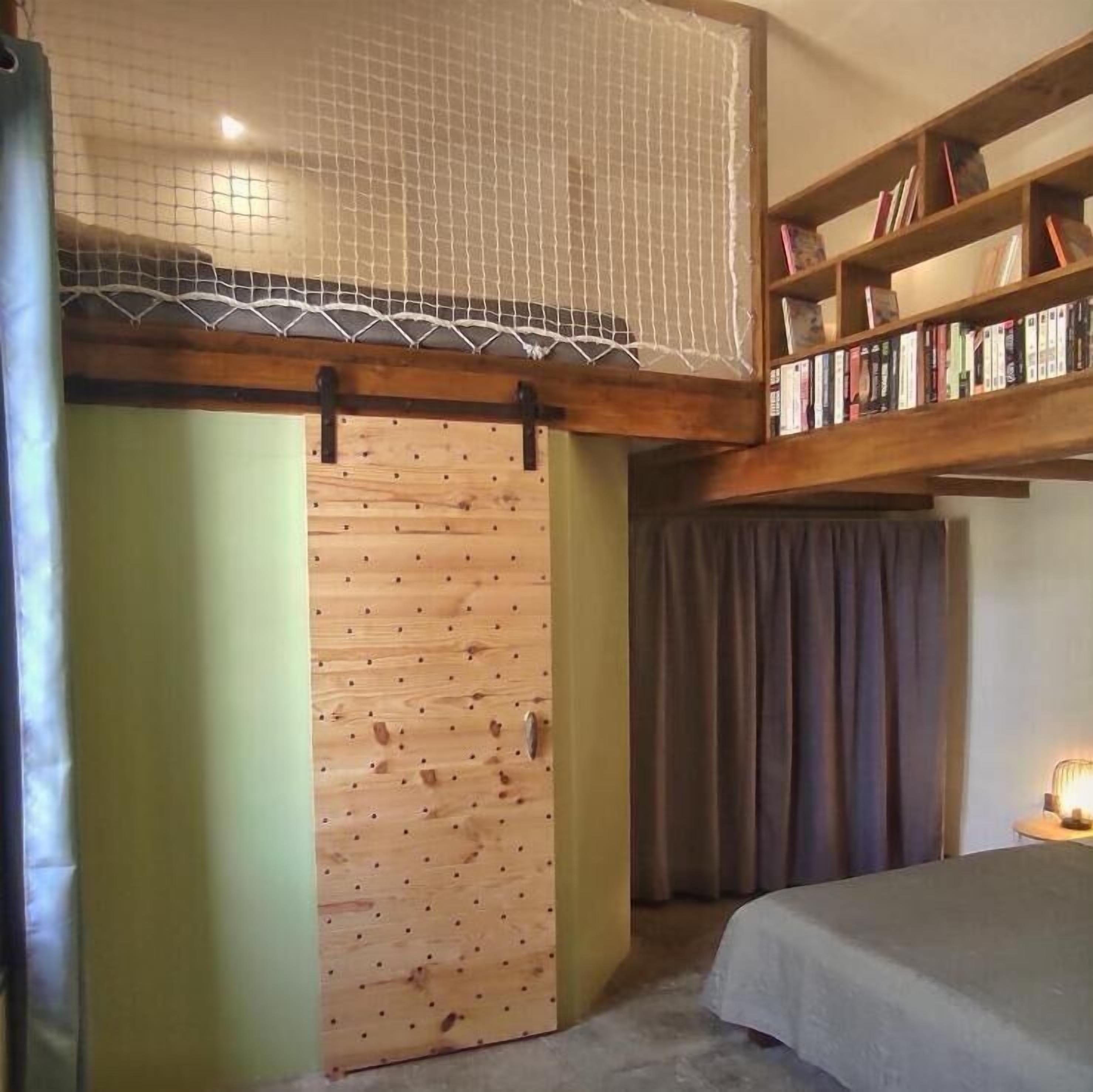 A room with a bunk bed, a wooden door, a bookshelf, and a curtain.