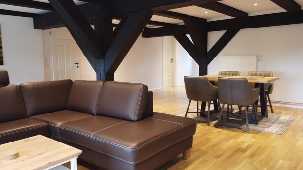 A modern living room with a brown leather sectional sofa, a wooden coffee table, and a dining area with a wooden table and chairs. - 1 Bedroom Apartment in Klein Upahl (Klein Upahl)