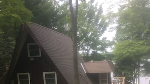 Une petite cabane de couleur sombre, dotée d’un toit à forte pente et d’un petit porche.