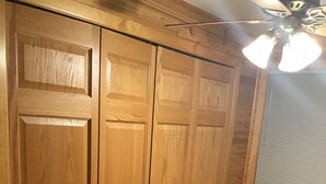 Une pièce aux murs recouverts de lambris en bois, dotée d’un ventilateur de plafond et d’une fenêtre avec des stores.