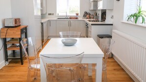 A modern kitchen with white cabinets, a wooden countertop, and a dining area with a white table and clear chairs. - Beach Apartment 9 (Holyhead)
