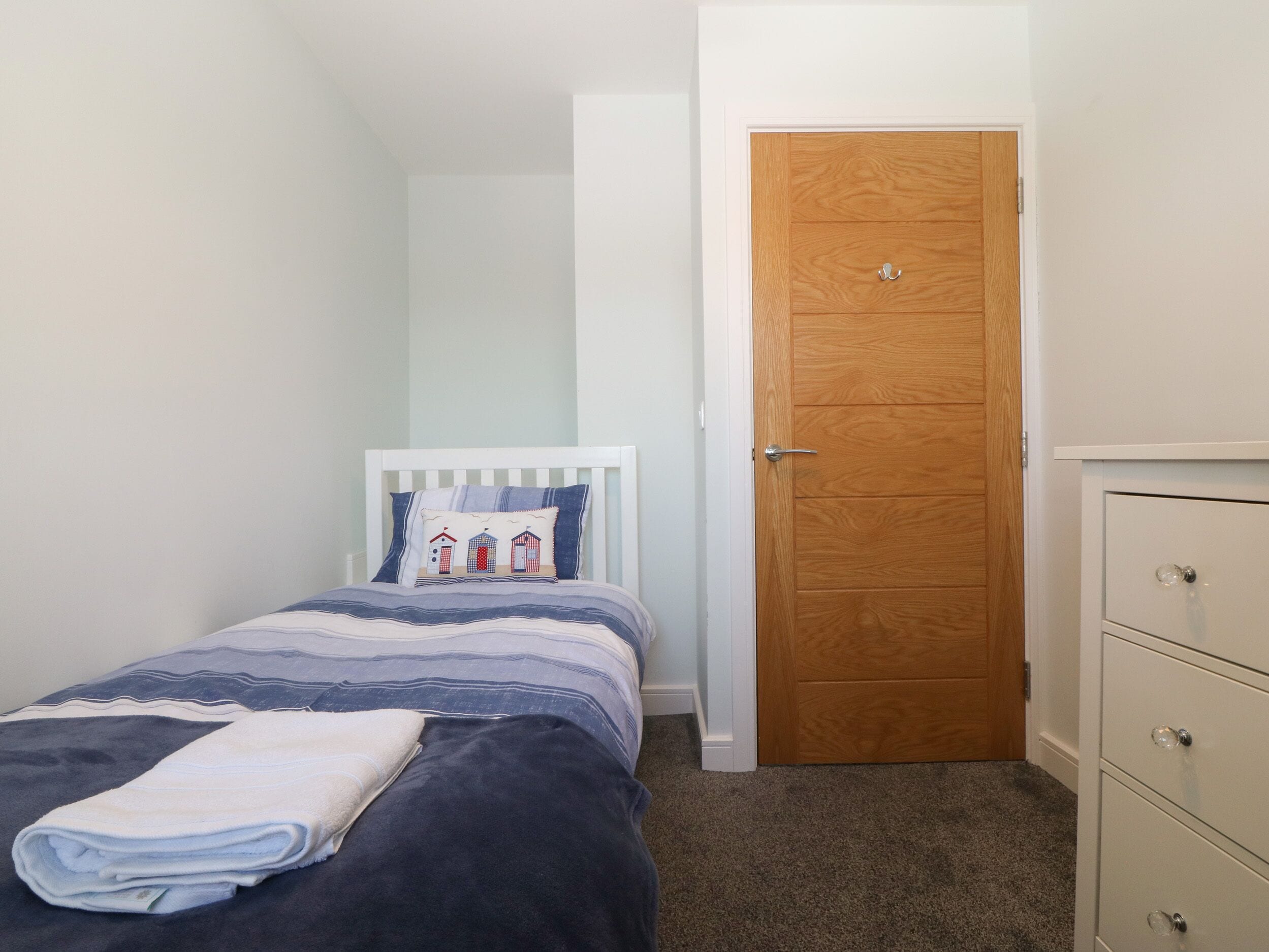 A small, neatly arranged bedroom with a single bed, a wooden door, and a dresser.