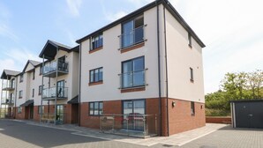 A multi-story residential building with a flat roof, large windows, and a brick facade. - Beach Apartment 9 (Holyhead)