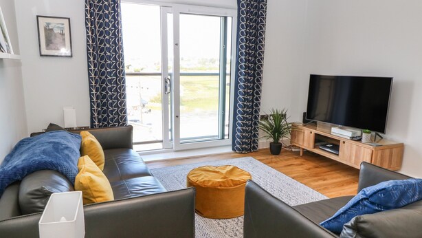 A modern living room with a sofa, ottoman, and a flat-screen TV on a wooden stand. - Beach Apartment 9 (Holyhead)