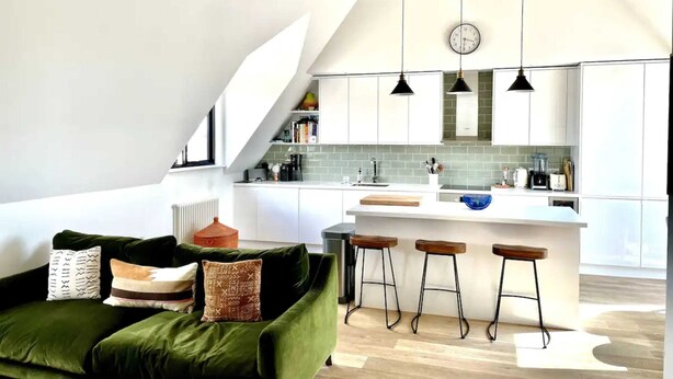 A modern kitchen with white cabinets, a wooden ceiling, and a bar area with stools. - Unique 2 Bedroom Penthouse Apartment in Kensal Rise (London)