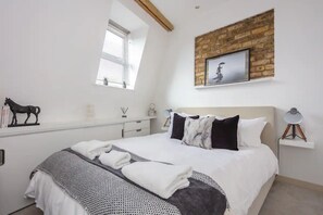 A bedroom with a bed, a window, a brick wall, and a picture frame.