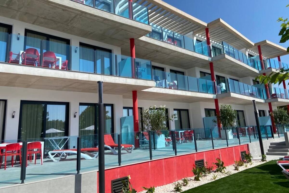 A modern hotel with a glass balcony, red chairs, and a pool area.