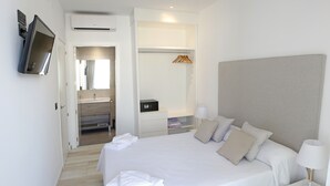 A hotel room with a large bed, bedside tables, a TV, a mirror, a bathroom with a sink and shower, and a wardrobe. - Azahar Beach Apartments (Alcala de Xivert)