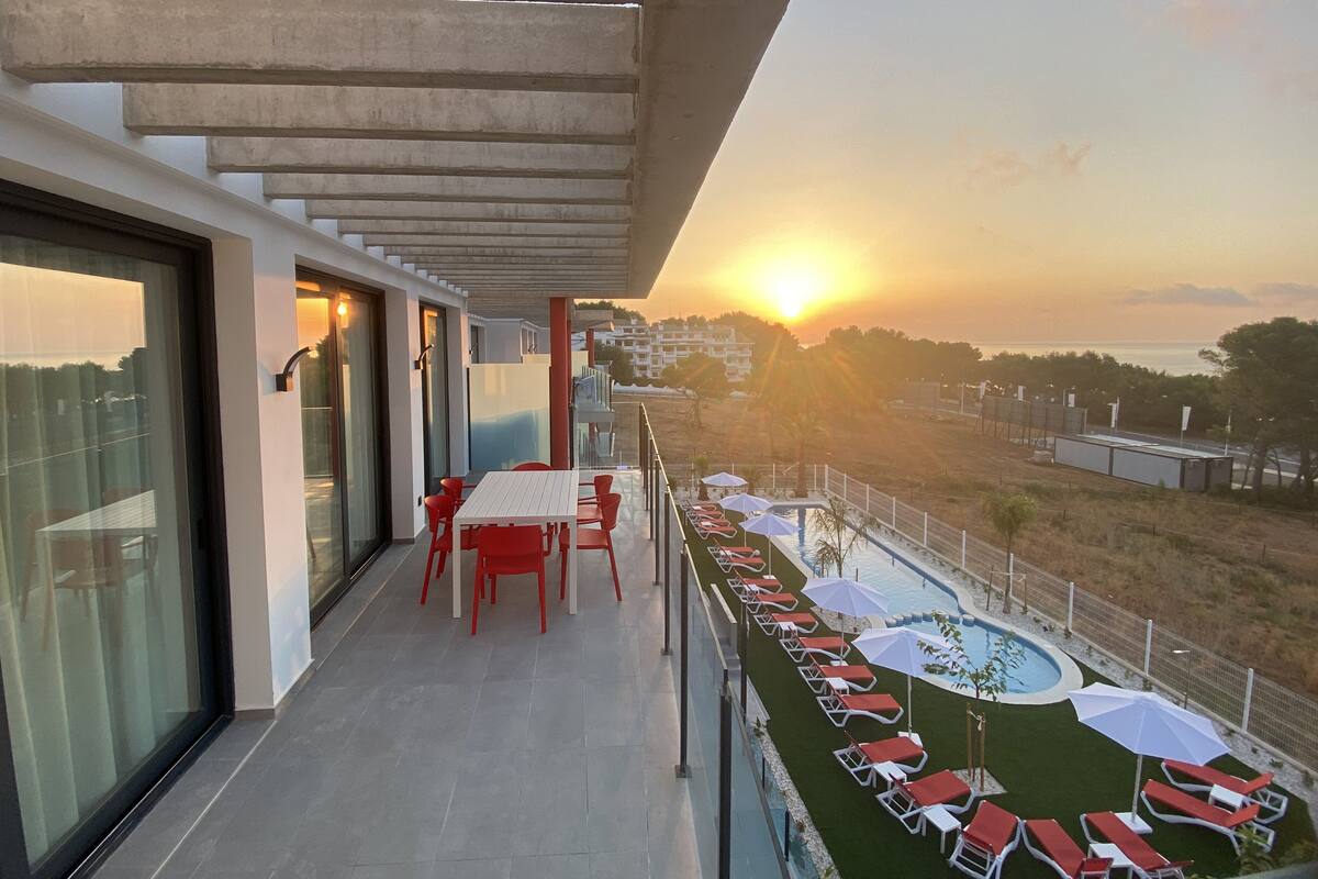 A balcony with a pool, red chairs, and umbrellas.