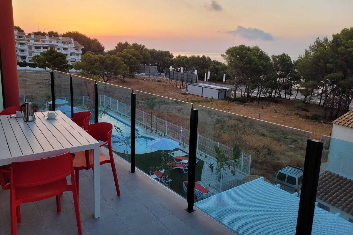 A balcony with a table and chairs, overlooking a swimming pool and a view of buildings and trees.
