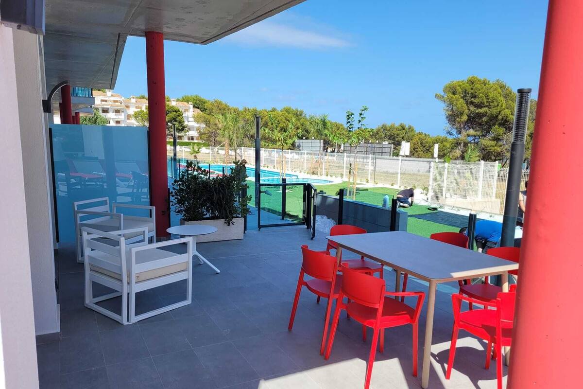 An outdoor patio with a table and chairs, a pool in the background, and a view of a residential area.