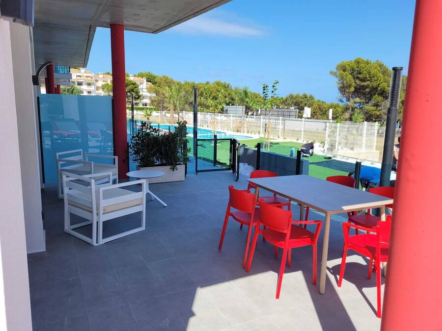 Un patio exterior con una mesa y sillas, una piscina al fondo y vistas a una zona residencial.