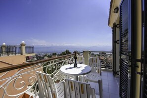 A balcony with a white table and chairs, overlooking a coastal view with buildings and mountains in the distance. - Filoxenia Kirki apartments (Corfu)