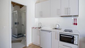 Eine kleine Küche mit weißen Schränken, einem Geschirrspüler, einem Einbauofen und einer Duschkabine aus Glas.
