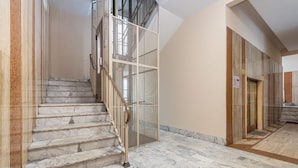 Una escalera de mármol con alfombra roja, barandilla de metal y panel de malla.