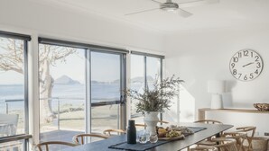 A dining area with a table, chairs, a clock, and a view of the sea. - Sandy Point Beach House - On The Waterfront.  Mid Week Stay Special Is Now On. (Corlette)