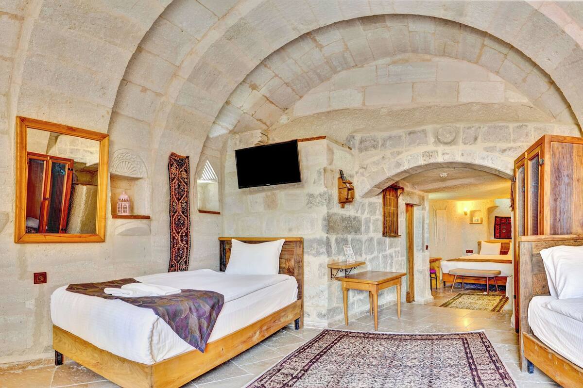 A room with two wooden beds, a flat-screen TV mounted on the wall, and a stone arch ceiling.