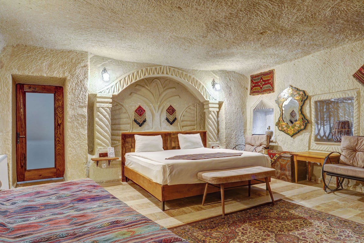 A bedroom with a wooden bed, a bench, a small table, a mirror, and a door.