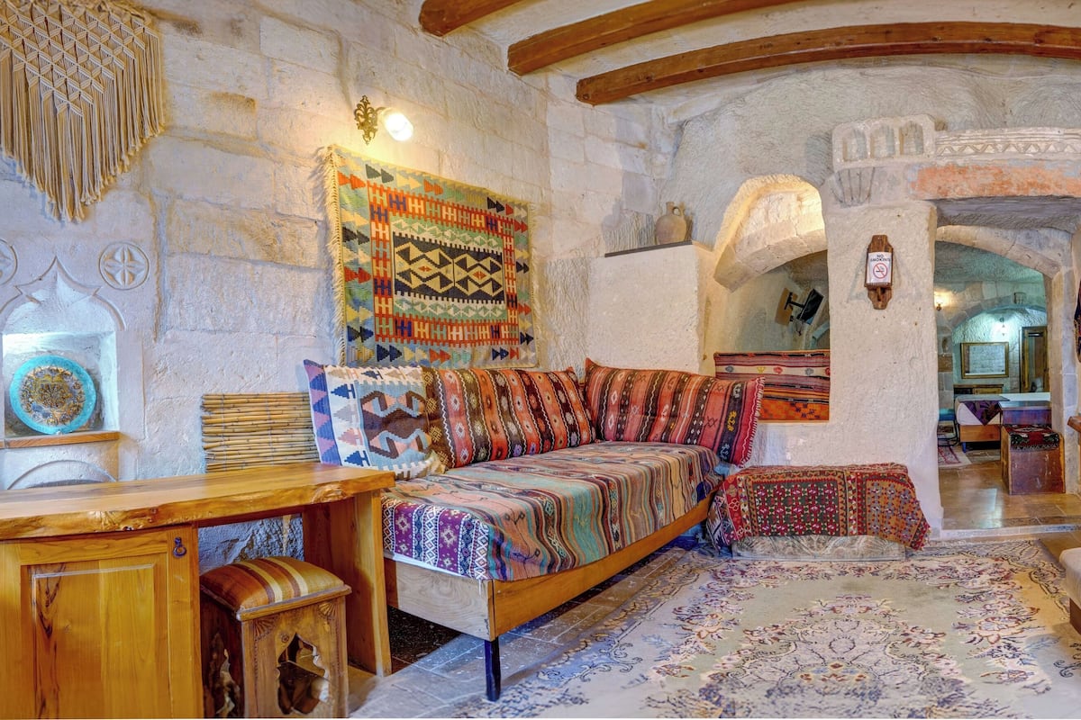 A cozy room with a wooden sofa, a patterned rug, and a stone wall.