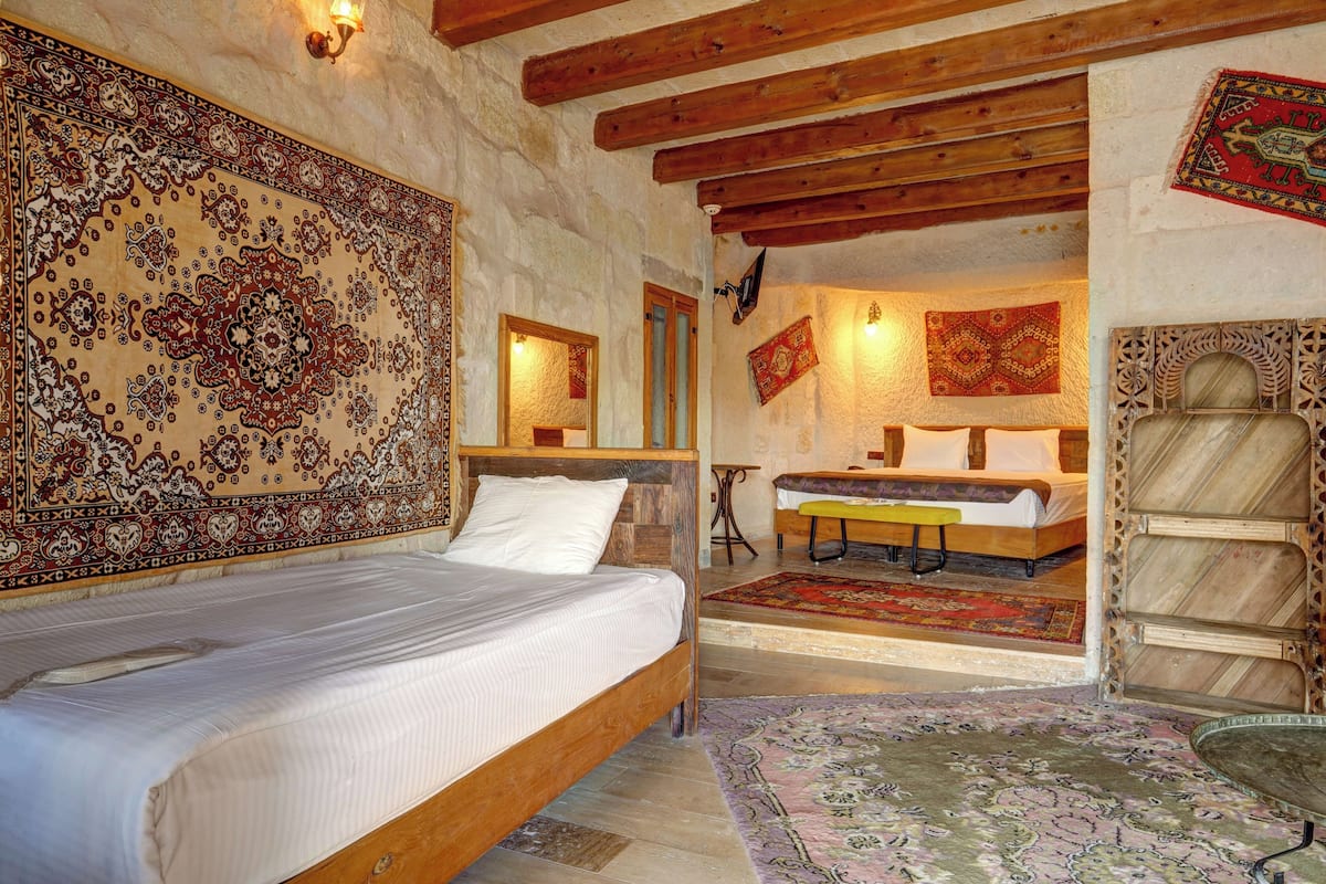 A bedroom with a wooden bed, a large patterned tapestry, and a small table with a chair.