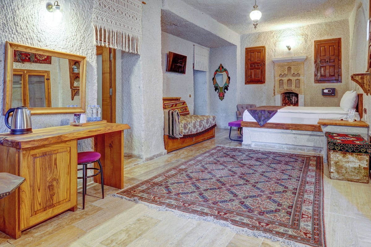 A cozy room with a wooden desk, a bed with a patterned bedspread, a decorative mirror, and a traditional rug.