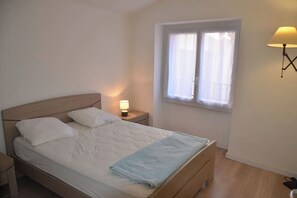 A neatly made bed with pillows, a bedside lamp, and a window with curtains.