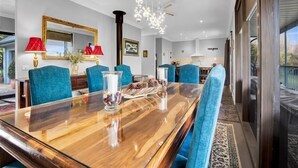 Een eetgedeelte met een grote houten tafel, blauwe stoelen met bekleding en een kroonluchter.