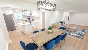 Eine moderne Küche mit weißen Schränken, einer zentralen Kochinsel und einem Essbereich mit Holztisch und blauen Stühlen.