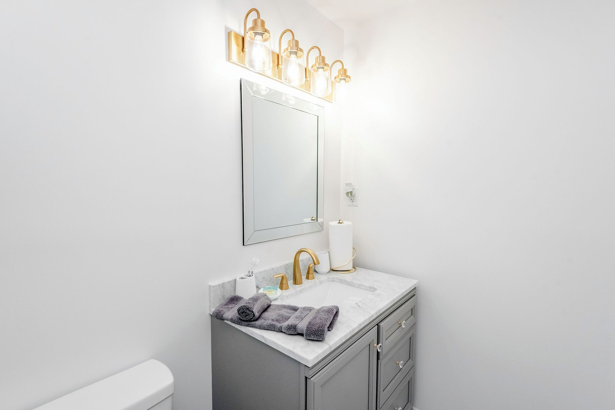 A bathroom with a white sink, gold faucets, and a mirror above it.