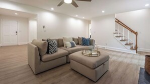 Ein modernes Wohnzimmer mit einem Ecksofa, einem runden Couchtisch und einem Deckenventilator.
