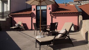 Terraza en la azotea con sillones de descanso, una mesa y una sombrilla.