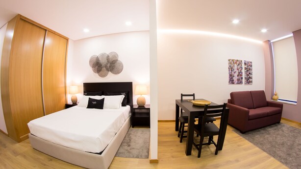 A modern hotel room with a large bed, a desk, a red sofa, and a dining area.