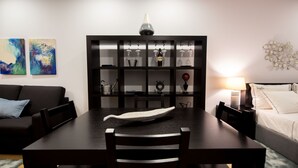 Uma área de jantar moderna com uma mesa de madeira escura, cadeiras e uma ilha central. Um vaso decorativo está sobre a mesa, e uma adega com copos e garrafas fica ao fundo.