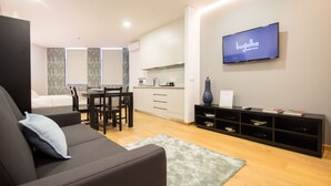 Uma sala de estar moderna com sofá, televisão na parede, área de jantar com mesa e cadeiras, e cozinha com armários e micro-ondas.