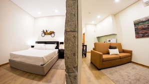 A bedroom with a bed, a nightstand, a wall-mounted clock, and a stone pillar. - Bugalha My Loft Douro 8 (Peso da Régua)