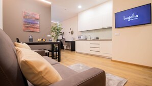 A modern living room with a sofa, a dining table with chairs, and a kitchen area with white cabinets and a TV displaying 'bugalha'. - Bugalha My Loft Douro 9 (Peso da Régua)
