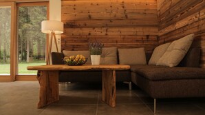 A modern living room with a wooden wall panel, a dark brown sofa, a wooden coffee table, and a floor lamp. - Ferienhaus mit Sauna am Waldrand (Kärnten)