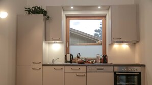 A modern kitchen with white cabinets, a built-in oven, and a window above the sink. - Ferienhaus mit Sauna am Waldrand (Kärnten)