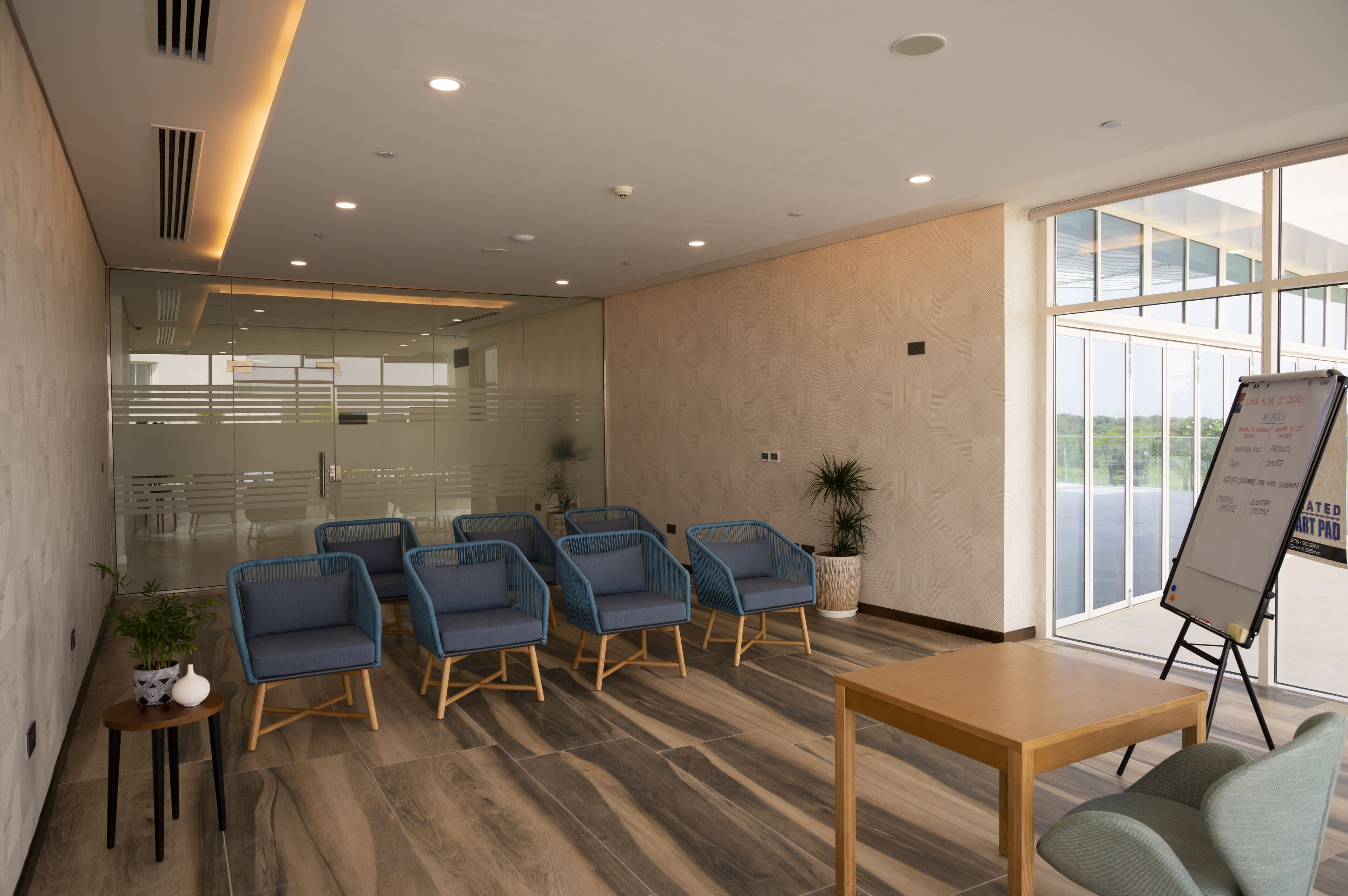 Un salón de conferencias moderno con mampara de vidrio, suelo de madera y sillas azules.