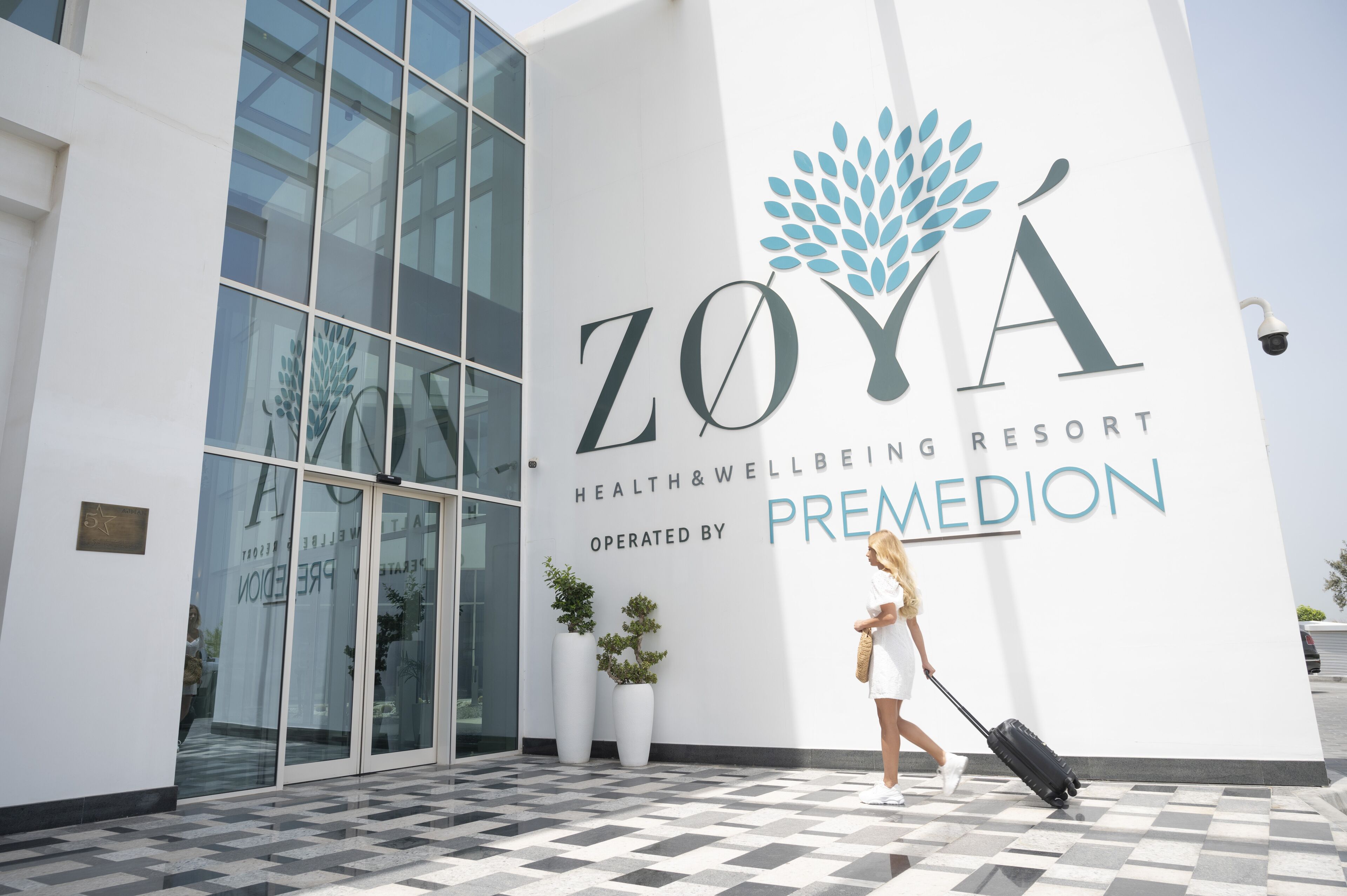 A modern building with a large glass entrance, a logo for Zoya Health & Wellness Resort, and a sign indicating it is operated by Premedian.